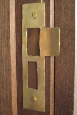 A shaped brass strike plate on a wood door frame